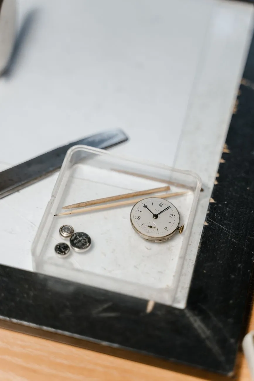 A small dial and parts in a clear tray on the bench